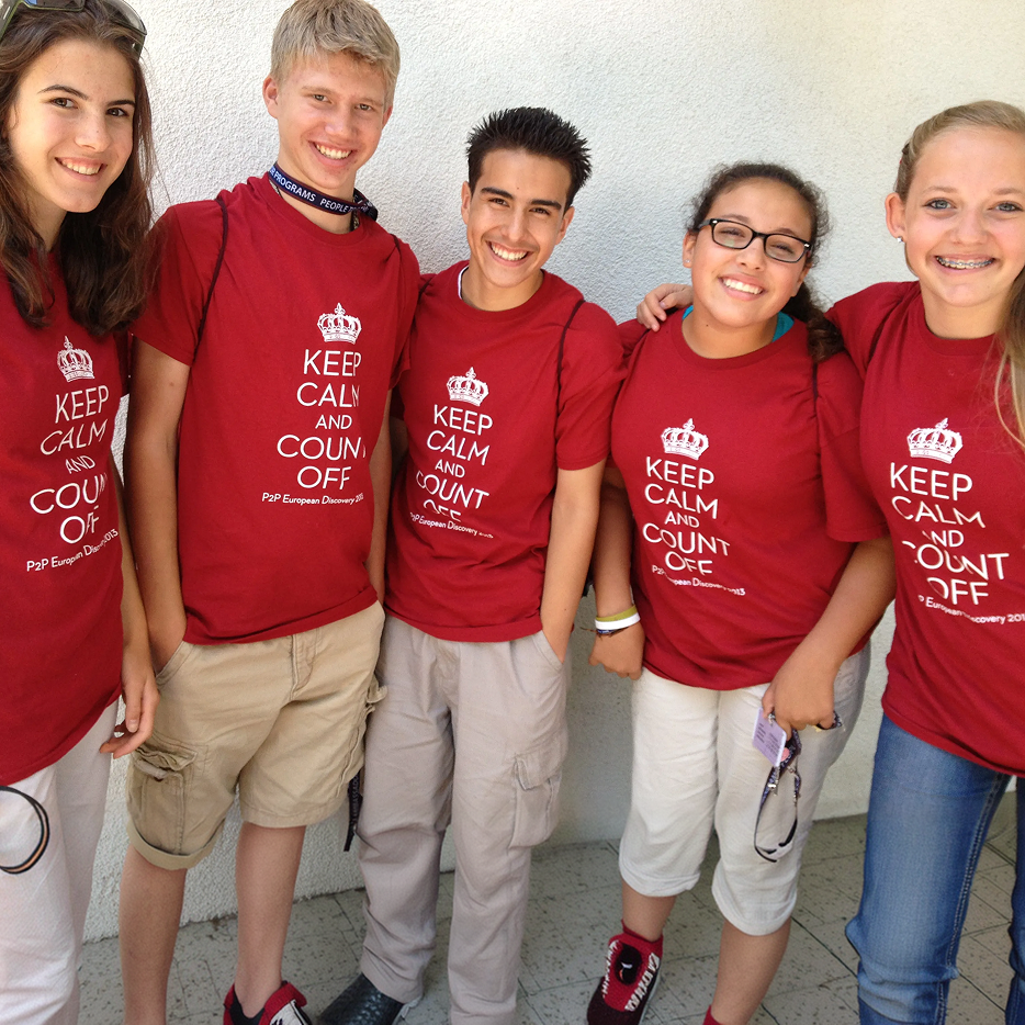 Five people wearing red shirts with a printed design, standing together against a light-colored wall.