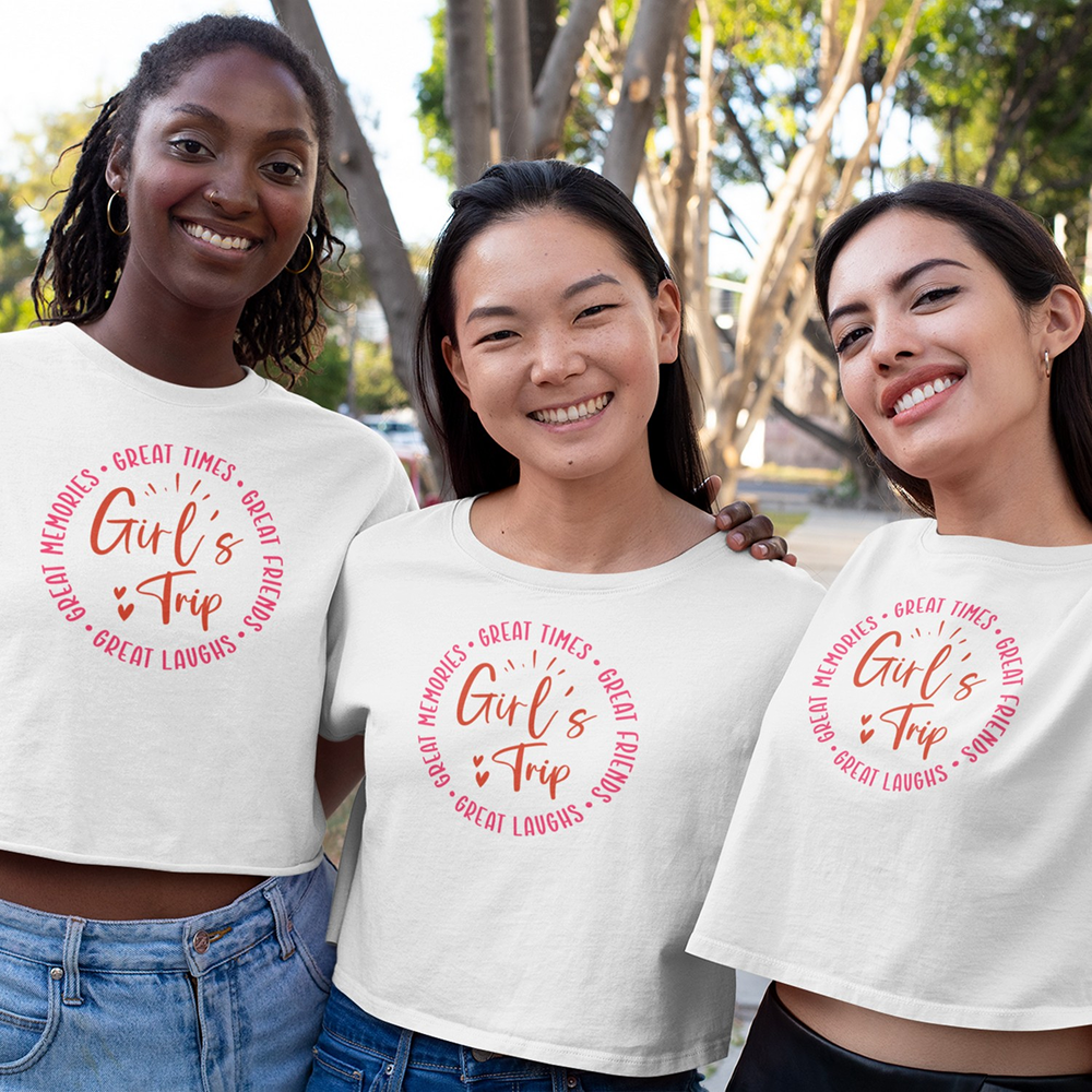 Three women wearing white t-shirts with 'Girl's Trip' text, standing outdoors.