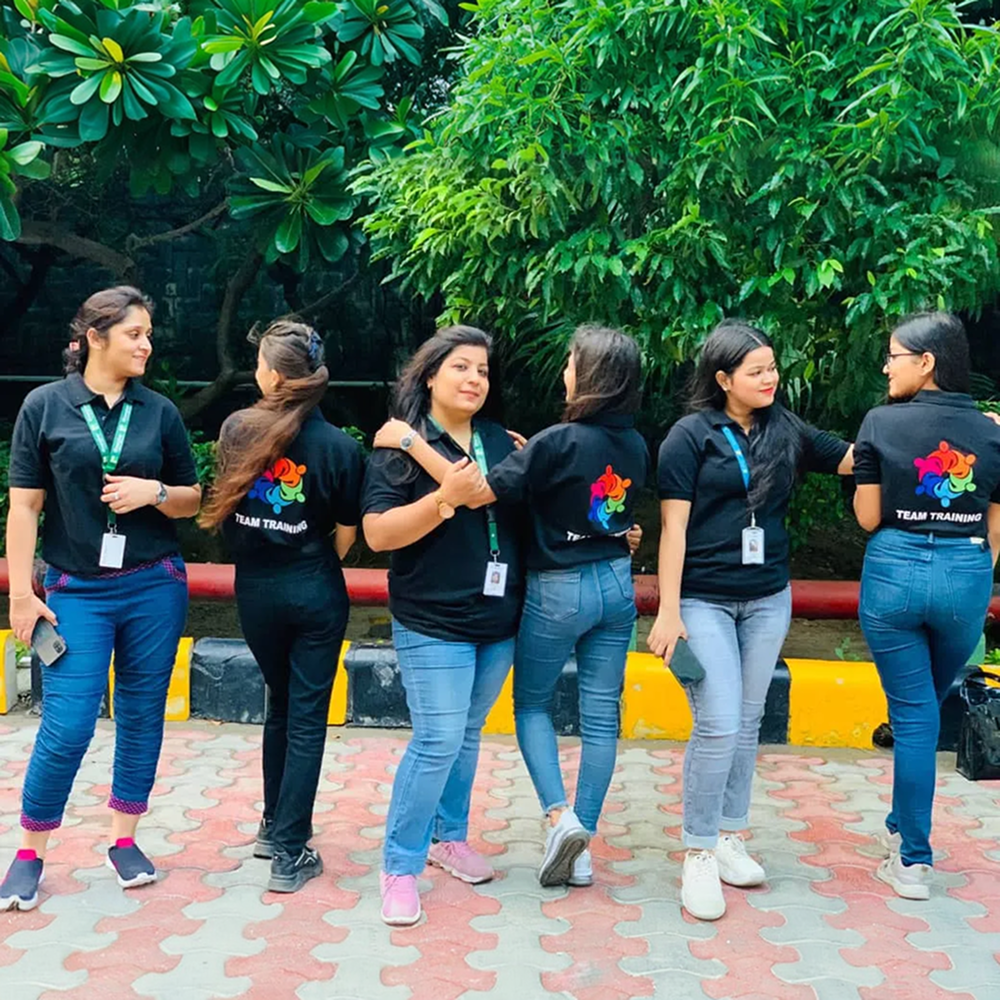 Group of women in matching black shirts with colorful logos and blue jeans standing outdoors.