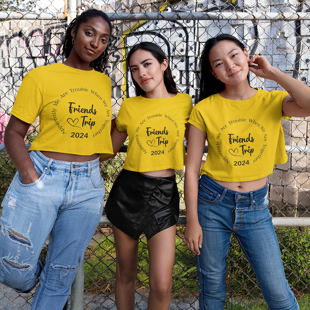 Three women wearing yellow t-shirts with 'Friends Trip 2024' text, standing in front of a chain-link fence.