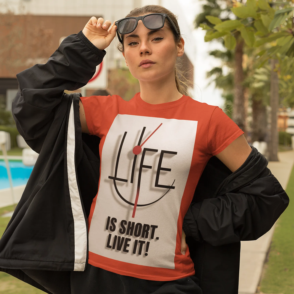 Person wearing a red t-shirt with 'LIFE IS SHORT. LIVE IT!' text, holding sunglasses, outdoors.