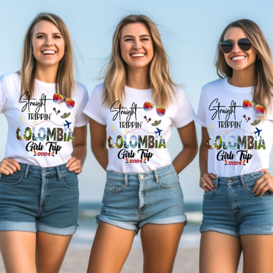 Three women wearing matching t-shirts with 'Straight Trippin Colombia Girls Trip 2024' text on a beach.