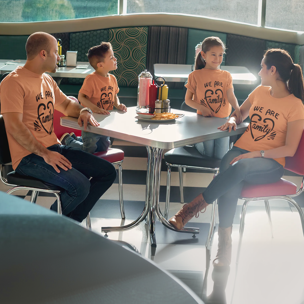 Family of four sitting at a table in a modern restaurant, all wearing matching 'We Are Family' shirts.