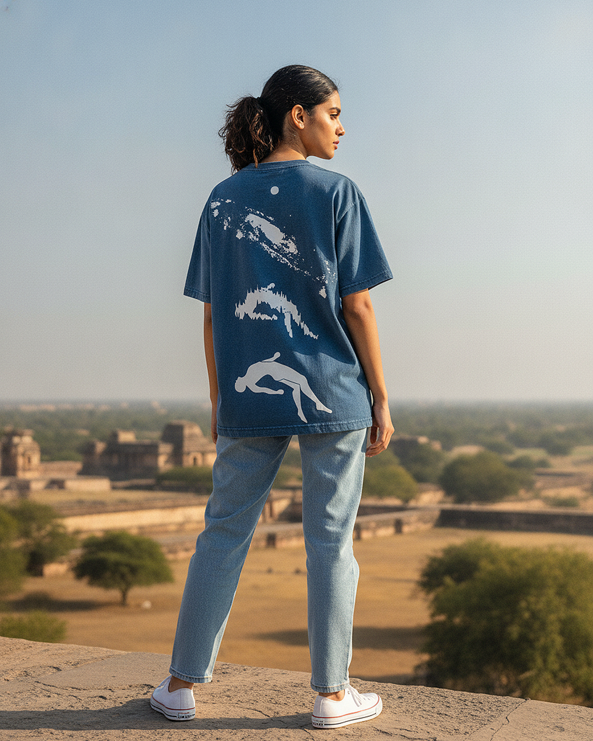 Girl wearing a Astral Drift Graphic Blue Boxy Fit T-Shirt with white graphics, standing on a high vantage point with a scenic view.