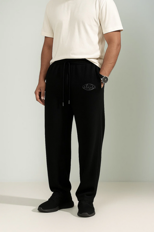 Person wearing black pants with a logo on a plain background