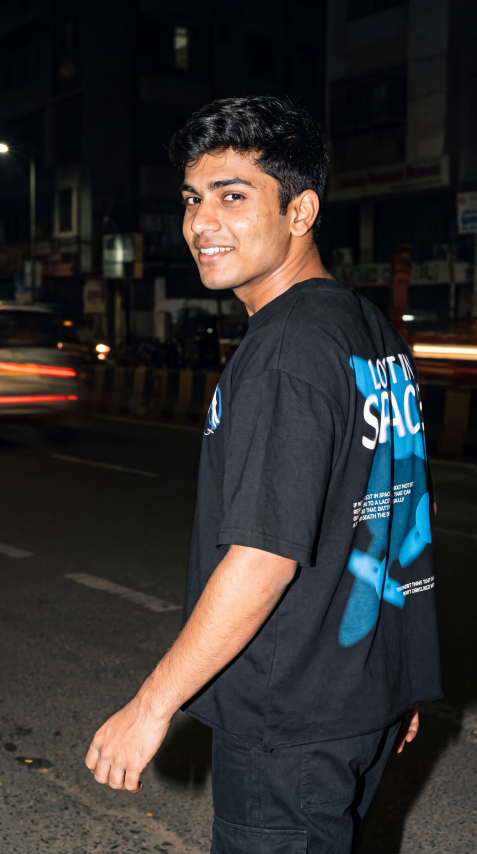 A man wearing a black t-shirt with a Scrollfit blue and white graphic print on the back, standing on a city street at night.