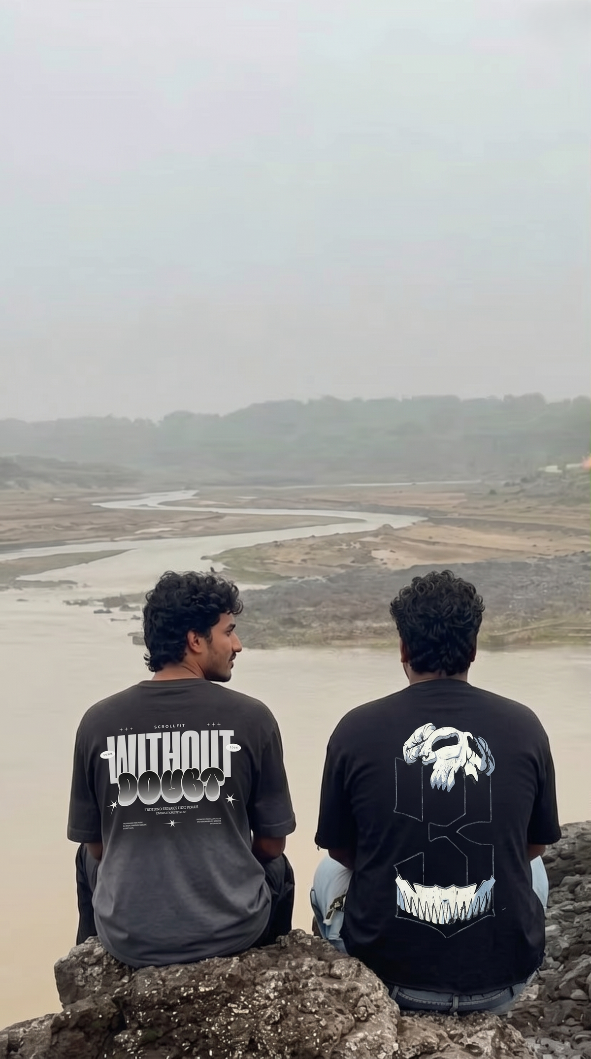 Two men sitting on rocks overlooking a river landscape, wearing Scrollfit black graphic t-shirts with white designs. The shirt on the left features the text 'WITHOUT BLOOD' and the shirt on the right features a large white skull graphic.