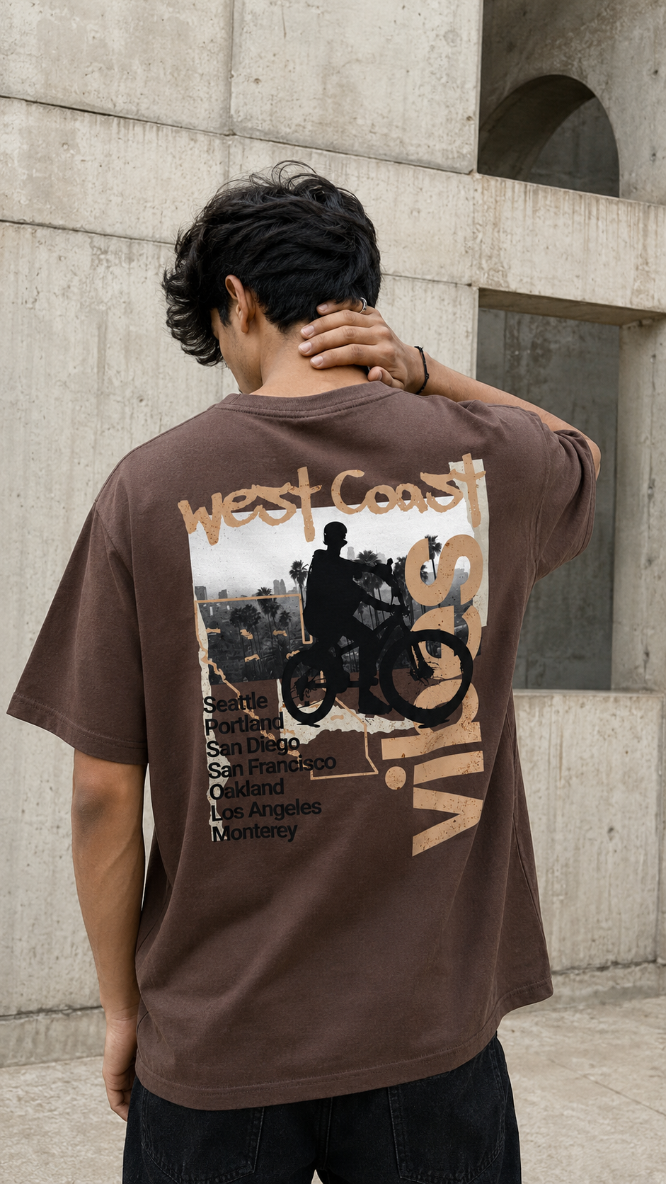 A man wearing a brown graphic t-shirt with a Scrollfit 'West Coast Vibes' motorcycle print, photographed from behind against a concrete wall.
