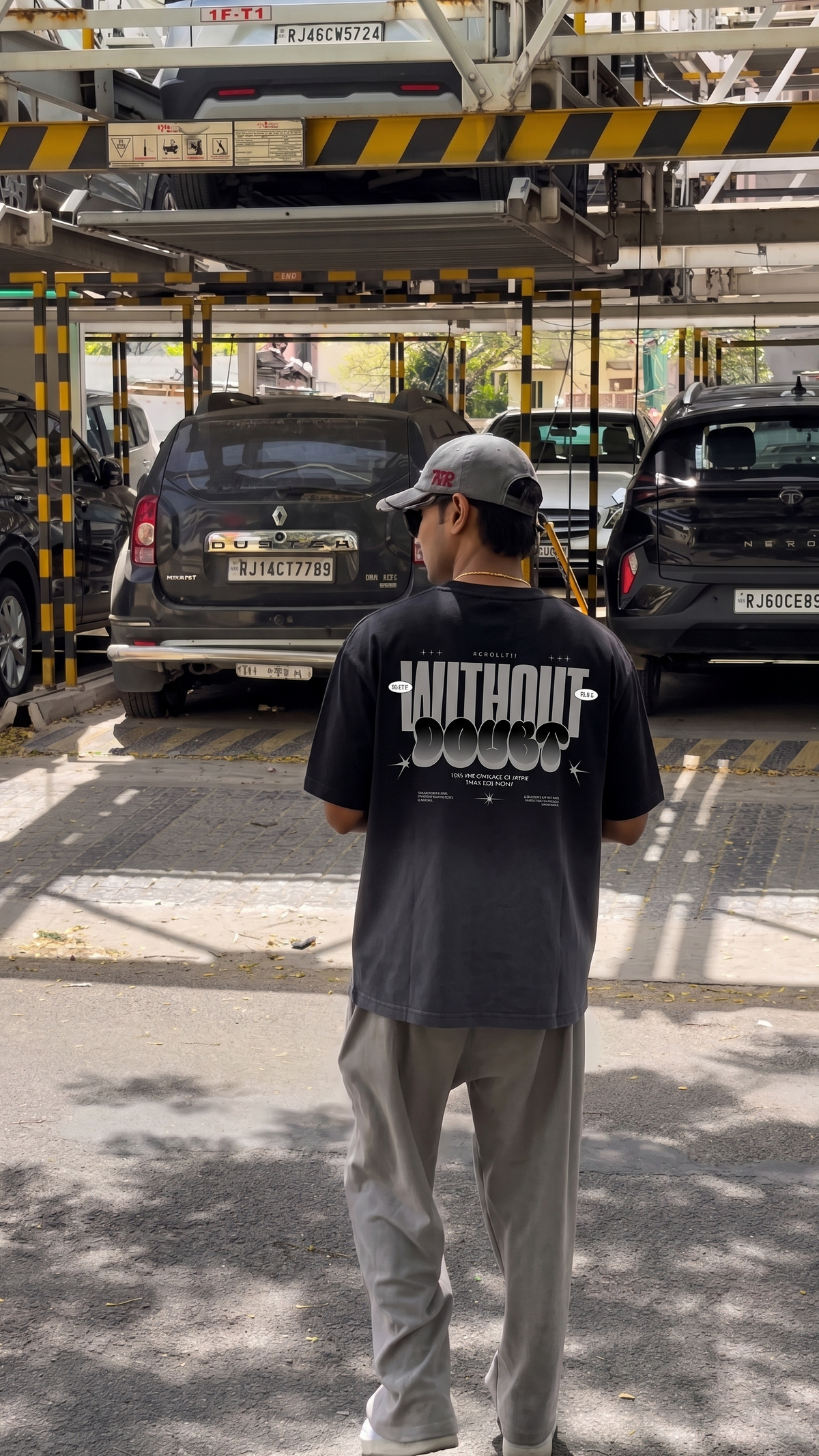 A man wearing a Scrollfit black t-shirt with a white graphic print that says 'WITHOUT DOUBT' and light gray sweatpants, standing in a parking structure.